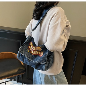 Detail view of washed denim crossbody bag featuring vintage embroidery and star patches
