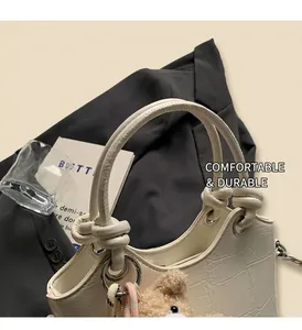 Detail of white crocodile pattern handbag with elegant knot handle and bear charm