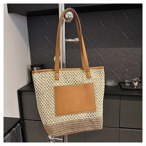 Detail of woven straw tote bag featuring brown leather straps and square front pocket design