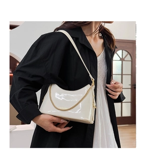 Detail of glossy white underarm bag featuring a thick gold chain and smooth mirror finish