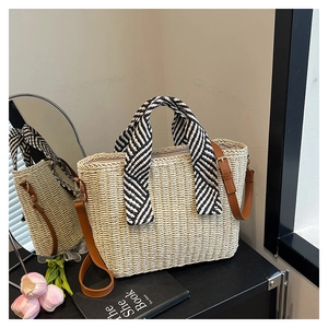 Détail d'un sac cabas en paille avec poignée en foulard et bandoulière sur bois sombre