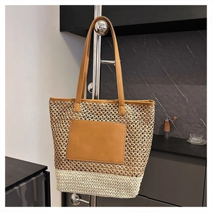 Detail of two-tone straw tote bag featuring brown leather patch and long shoulder straps