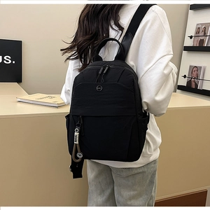 Detailed side view of minimalist black nylon backpack with metal logo and charm