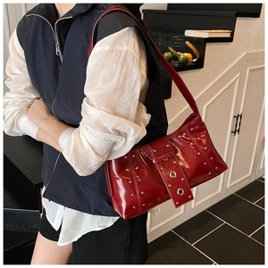 Détail d'un sac à bandoulière en cuir verni rouge foncé avec rivets et boucle en métal