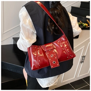 Détail du sac bandoulière en cuir verni rouge avec rivets argentés et boucle punk