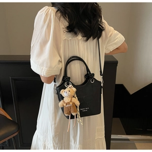 Close-up of black crocodile pattern handbag with a cute brown teddy bear keychain charm