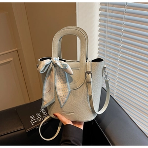 Dettaglio della borsa a secchiello azzurra con trama litchi e foulard su sfondo chic