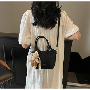 Detail of crocodile embossed bucket bag with plush bear charm worn on white dress
