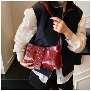 Détail du sac à bandoulière bordeaux avec rivets, texture brillante et œillets en métal