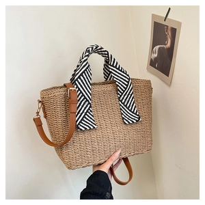 Détail du sac cabas en paille tissée avec bandoulière en cuir brun et foulard rayé