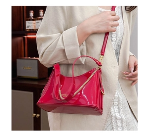 Red patent leather shoulder bag with gold chain strap worn in a luxury setting