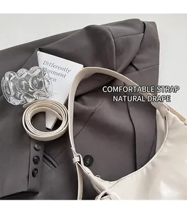 Gros plan du sac en cuir crème avec bandoulière réglable sur un blazer gris