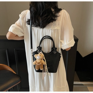 Detail of black crocodile texture bucket bag with a cute bear charm on a white lace dress