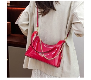 Close-up of a glossy red patent leather tote bag with gold chain and logo on a model