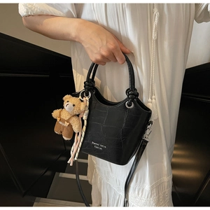 Detail of black crocodile texture handbag with plush bear charm and round handles