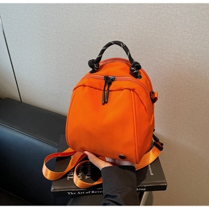 Detail of orange waterproof mini backpack with woven handle on a black leather sofa