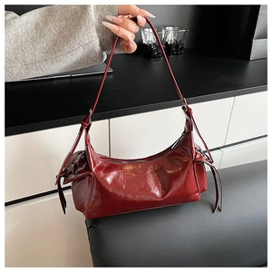 Détail du sac à épaule en cuir verni rouge foncé avec œillets métalliques et cordons latéraux
