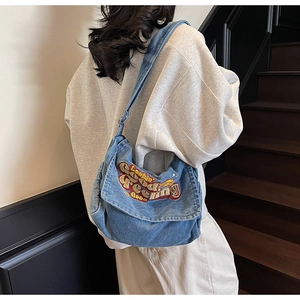 Detail of blue denim tote bag featuring Looking Feeling Good colorful embroidery