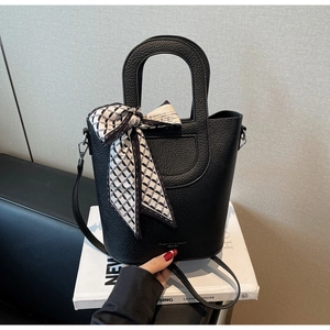 Dettaglio della borsa a secchiello in pelle nera con foulard e accessori metallici