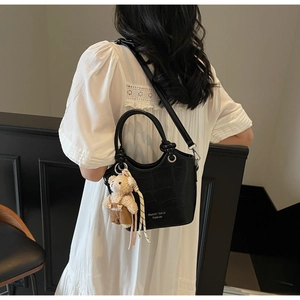 Detail of black crocodile texture handbag with a cute bear pendant on a white dress
