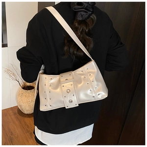 Détail d'un sac porté épaule beige avec rivets argentés et grands œillets métalliques