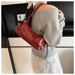 Modèle portant un sac sous le bras en cuir verni rouge foncé au fini brillant