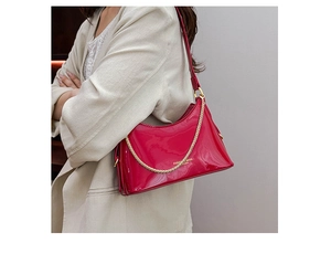 Detail of red patent leather bucket bag with gold chain decoration on white blazer