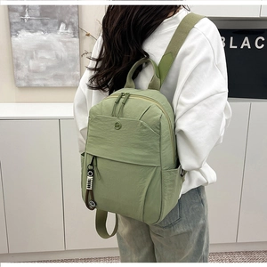 Rear view of a light green nylon backpack with metal logo and monochrome pendant