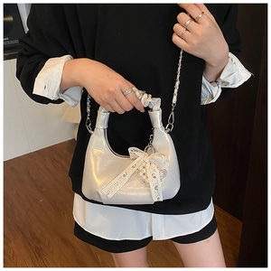 Detail of a pearl white pleated handbag with lace bow and pearl charm worn on shoulder