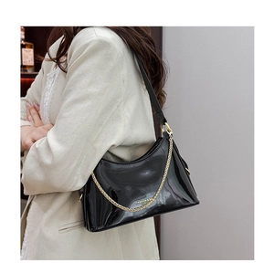 Close-up of black patent leather hobo bag with gold chain and leather shoulder strap