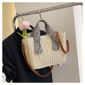 Détail d'un sac cabas en paille tressée beige avec anses à rayures et bandoulière brune