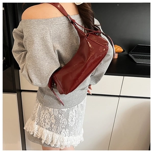 Détail d'un sac à bandoulière cylindrique en cuir verni bordeaux avec nœud sur l'anse