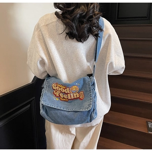 Close-up of embroidered stars and colorful text on washed blue denim tote messenger bag