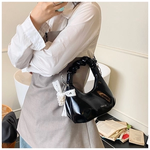 Detail of glossy black pleated handbag with pearl chain and lace bow accessories