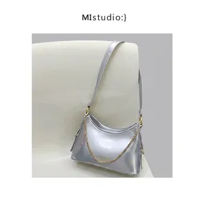 Detail view of silver patent leather shoulder bag with gold chain and metal finish