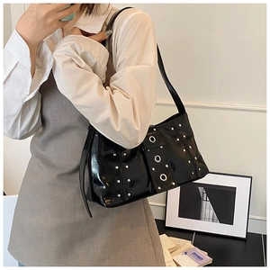 Détail d'un cabas vintage en cuir verni noir avec des clous argentés et des œillets