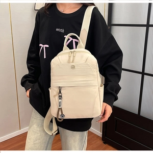 Detail of a beige minimalist backpack featuring a large zipper pocket and round logo badge