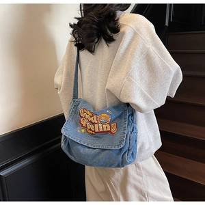 Detail of blue denim tote bag with Lookin Good Feeling Good embroidery on the flap