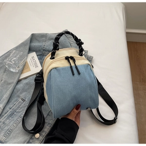 Detail of a color-block denim and cream mini backpack with nautical rope handle on a bed