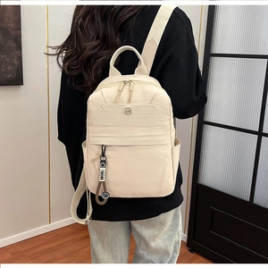 Detail of minimalist beige nylon backpack showing front zip pocket and cute pendant