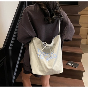 Détail du sac cabas en toile blanc cassé avec texte bleu et cordon de serrage décoratif en nœud