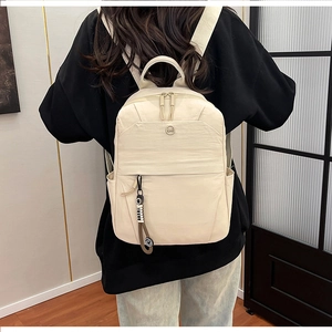 Detail of a beige nylon casual backpack with letter charm pendant shown in back view