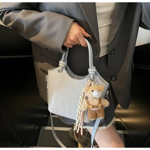 Detail of light blue crocodile texture handbag with cute plush bear charm on PU leather