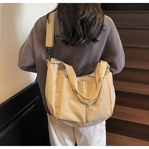 Detail of beige nylon crossbody bag showing dual front pockets and wide shoulder strap
