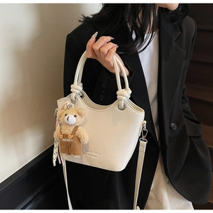 Close-up of white crocodile pattern bucket bag with cute plush bear pendant details