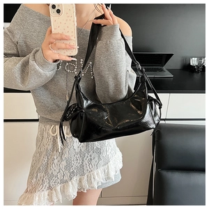 Détail du sac à bandoulière en cuir verni noir avec cordons décoratifs sur les côtés