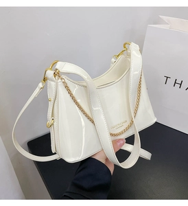 Close-up of white patent leather bucket bag with elegant gold chain strap and luxury texture