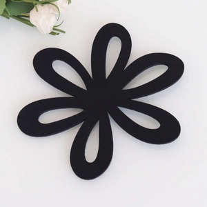Minimalist black floral felt coaster with hollow petal design on white surface