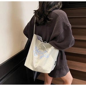 Détail du sac cabas en toile avec texte bleu, cordon de serrage et doublure à carreaux
