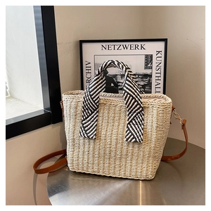 Détail d'un sac cabas en paille avec anses noires et blanches et bandoulière en cuir
